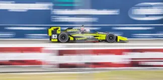 En gul och svart IndyCar-bil kör snabbt på en racerbana med suddig bakgrund.