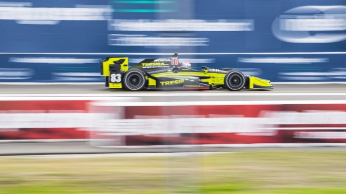 En gul och svart IndyCar-bil kör snabbt på en racerbana med suddig bakgrund.