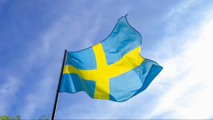 Sveriges flagga vajar mot en blå himmel.