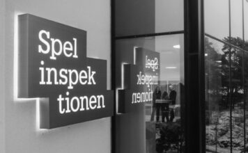 Skylt med texten Spelinspektionen utanför en byggnad, speglas i fönsterglas med personer synliga inomhus.
