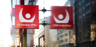 Svenska Spels logotyp på en skylt utanför en glasfasad med reflektion i fönstret.