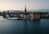 Vy över Riddarholmen i Stockholm med Riddarholmskyrkan och vatten i förgrunden vid skymning.