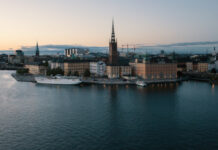 Vy över Riddarholmen i Stockholm med Riddarholmskyrkan och vatten i förgrunden vid skymning.