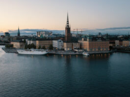 Vy över Riddarholmen i Stockholm med Riddarholmskyrkan och vatten i förgrunden vid skymning.
