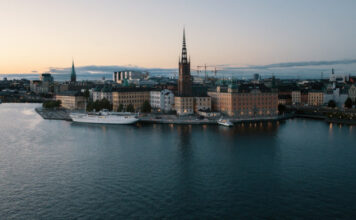 Vy över Riddarholmen i Stockholm med Riddarholmskyrkan och vatten i förgrunden vid skymning.