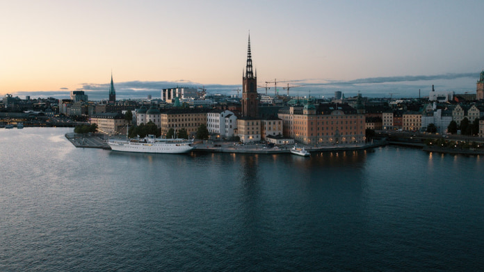 Vy över Riddarholmen i Stockholm med Riddarholmskyrkan och vatten i förgrunden vid skymning.