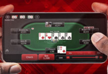 Två händer håller en mobil med ett pokerbord på skärmen och flera spelare runt bordet.