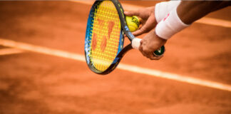 En tennisspelare förbereder sig för att serva på en grusbana med racket och boll i handen.