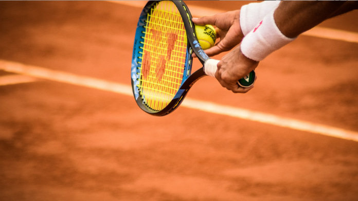 En tennisspelare förbereder sig för att serva på en grusbana med racket och boll i handen.