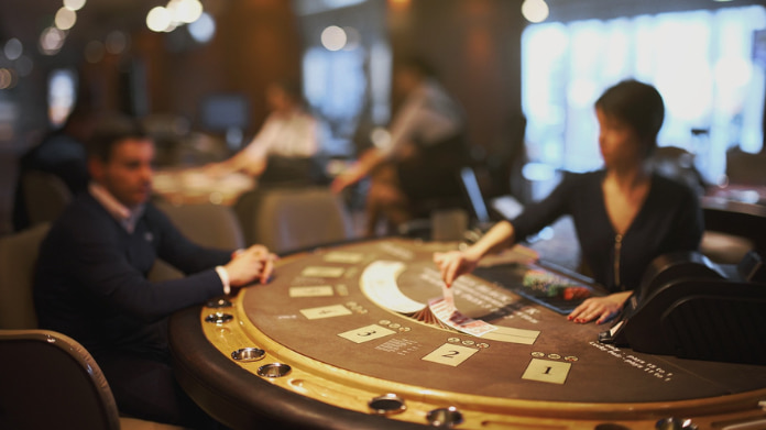 Två personer spelar kort vid ett kasinobord i en stämningsfull och upplyst spelmiljö.
