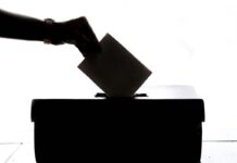 a shadowed hand placing a ballot in a voting box