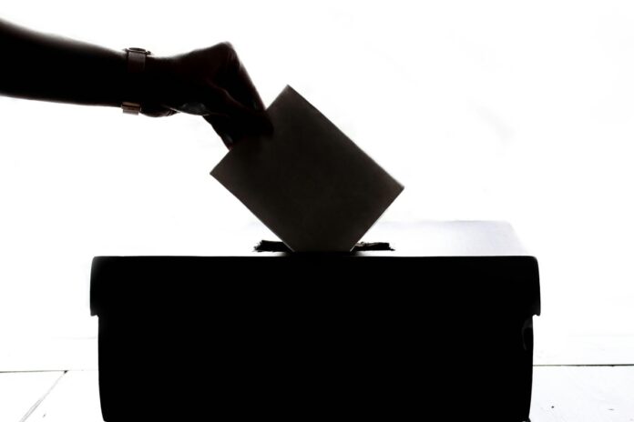 a hand placing a vote a shadowed hand placing a ballot in a voting box