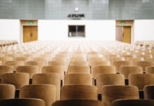 Empty college lecture hall with rows of wooden chairs facing a podium