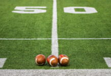 Three footballs placed on the 50-yard line of a football field.