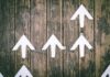 White upward-pointing arrows arranged on a wooden surface, symbolizing growth or positive direction.