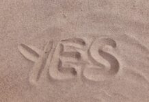 The word "YES" written in smooth, light brown beach sand.